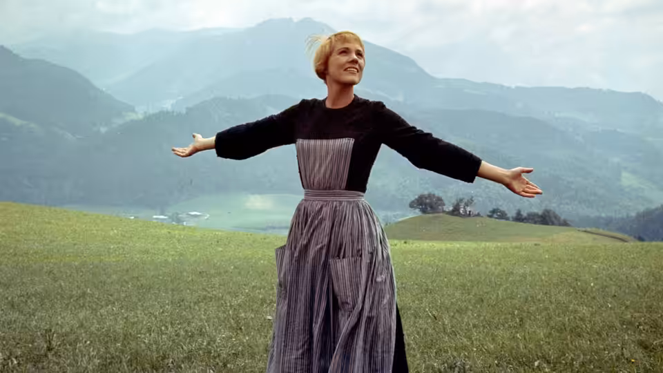 Maria (Julie Andrews) stands with arms outstretched in a mountain meadow