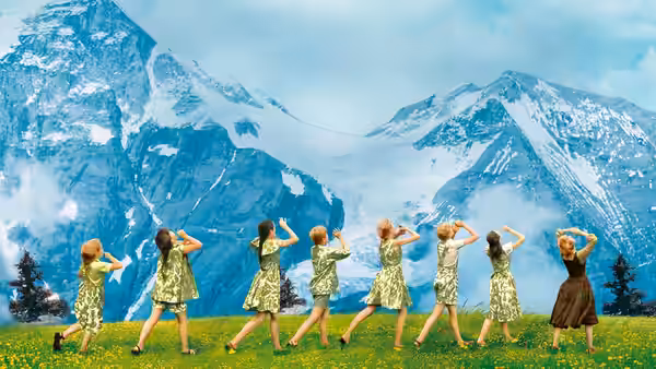 Children in matching outfits dance in a line across a mountain meadow