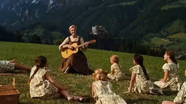 Maria (Julie Andrews) plays guitar for children seated on a grassy hillside