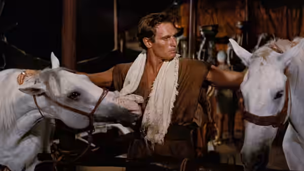 Judah Ben-Hur (Charlton Heston) stands between two white horses in a stable