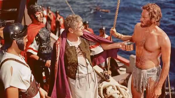 Quintus Arrius (Jack Hawkins) offers a cup to a man on a Roman ship