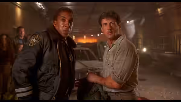 Kit Latura (Sylvester Stallone) and George Tyrell (Stan Shaw) stand among damaged vehicles underground