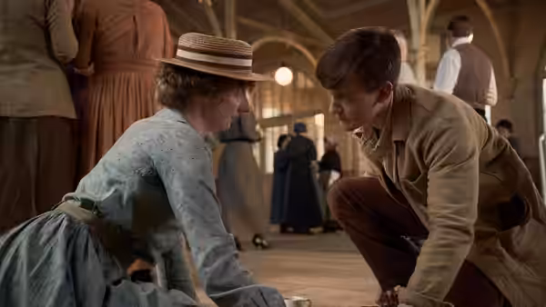 A young woman and man crouch facing each other on the floor of a hall