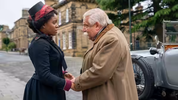 Mary Lockwood (Amara Okereke) speaks with an older man beside a parked car