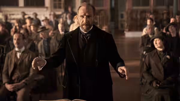 Dr. Henry Guthrie (Ralph Fiennes) conducts a seated choir in a crowded hall