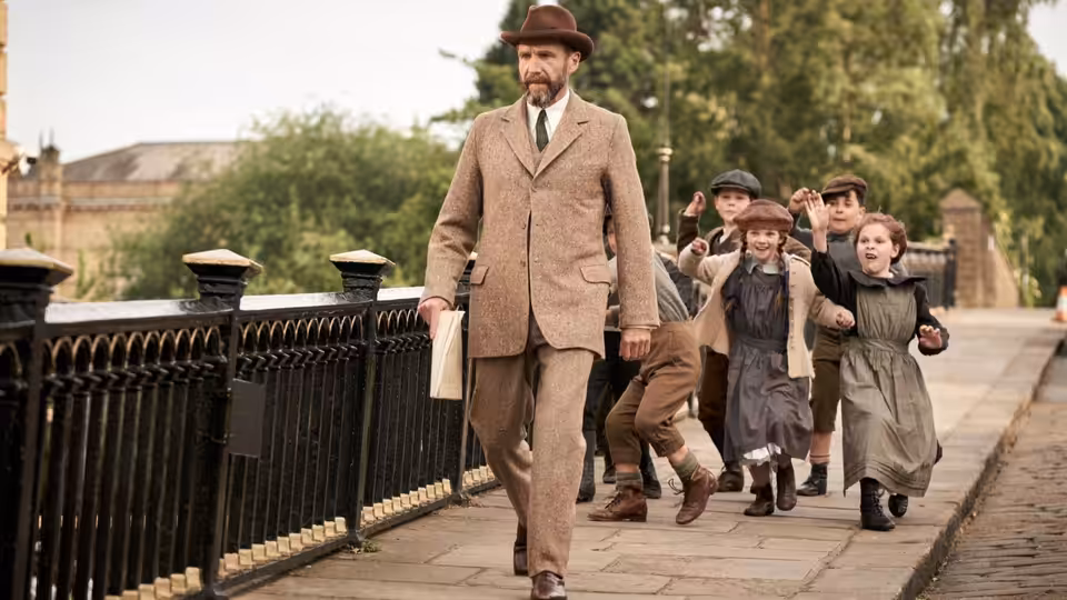 Dr. Henry Guthrie (Ralph Fiennes) walks along a riverside path as children follow behind