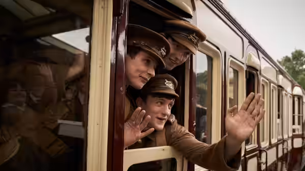 Young uniformed men lean from a train window and wave goodbye