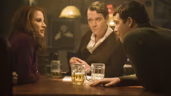 Young Rachel Singer (Jessica Chastain), Young David Peretz (Sam Worthington), and Young Stefan Gold (Marton Csokas) sit around a bar table