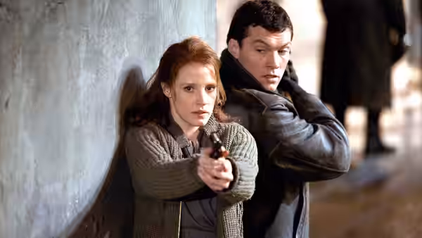 Young Rachel Singer (Jessica Chastain) aims a handgun from behind a wall as Young David Peretz (Sam Worthington) watches