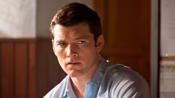 Young David Peretz (Sam Worthington) sits indoors in a pale blue shirt