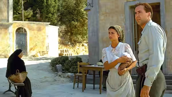 Pelagia (Penélope Cruz) and Dr. Iannis (John Hurt) stand outside their home as a woman sits nearby