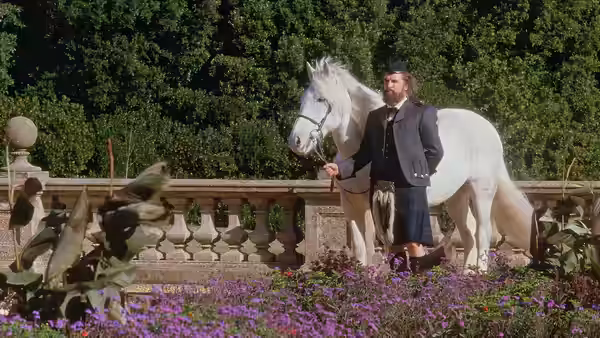 John Brown (Billy Connolly) holds a white horse on a garden terrace among flower beds