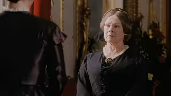 Queen Victoria (Judi Dench) faces a woman in dark mourning dress inside a richly decorated room