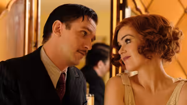 Charles Condomine (Dan Stevens) and Ruth Condomine (Isla Fisher) exchange glances at a gathering