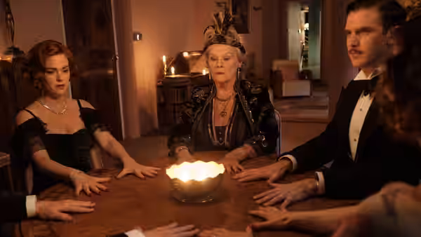 Madame Arcati leads a séance as Charles and a red-haired woman sit around the table