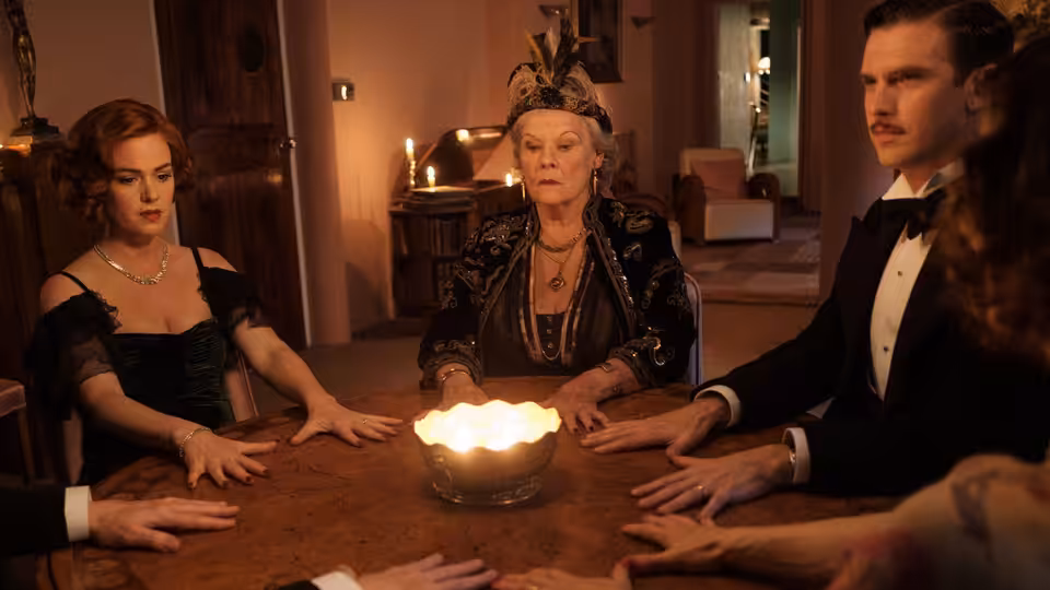 Madame Arcati leads a séance as Charles and a red-haired woman sit around the table