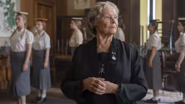 Miss Rocholl (Judi Dench) stands among uniformed students inside a school hall