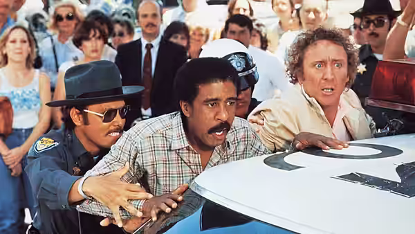 Harry Monroe (Richard Pryor) and Skip Donahue (Gene Wilder) scramble over a car as an officer restrains them
