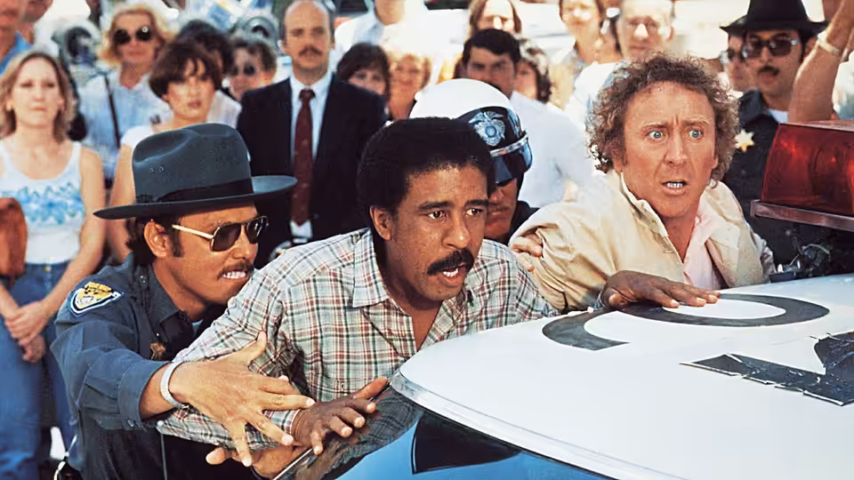 Harry Monroe (Richard Pryor) and Skip Donahue (Gene Wilder) scramble over a car as an officer restrains them