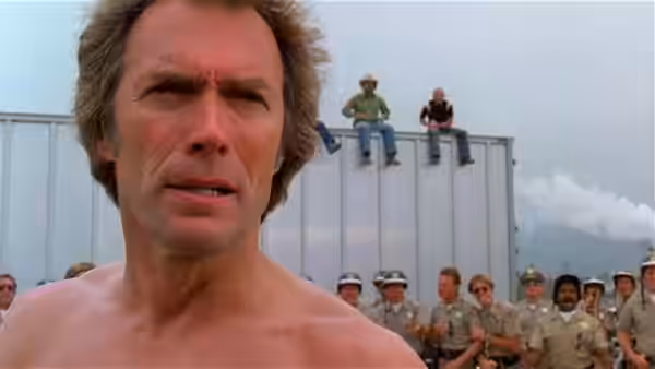 A shirtless Philo Beddoe (Clint Eastwood) stands before a crowd of uniformed men