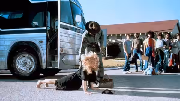 Judy Benjamin (Goldie Hawn) crawls beside a bus as soldiers gather behind her