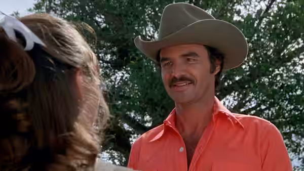 Bandit (Burt Reynolds) smiles at a woman beneath the trees