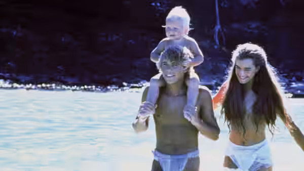 Richard (Christopher Atkins) carries their child on his shoulders as Emmeline (Brooke Shields) walks beside them
