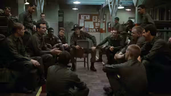 Sgt. Hulka (Warren Oates) sits among recruits gathered in a barracks room