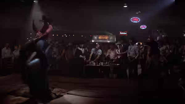 A cowboy rides a mechanical bull as honky-tonk patrons watch from around the arena