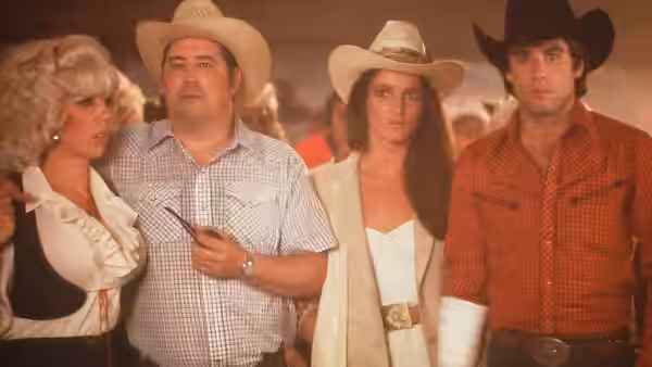 Sissy (Debra Winger) and Bud Davis (John Travolta) stand with companions inside the honky-tonk