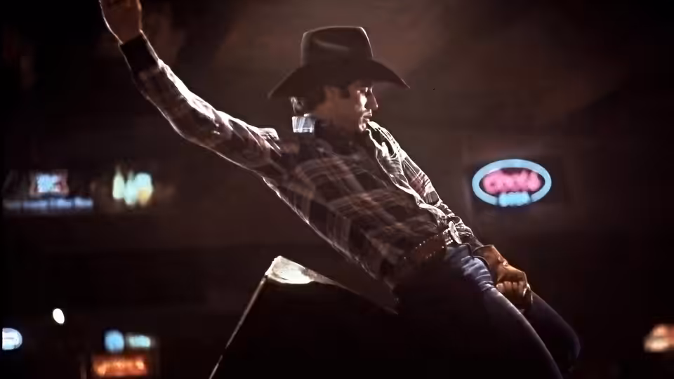 Bud Davis (John Travolta) rides a mechanical bull beneath the lights of a honky-tonk