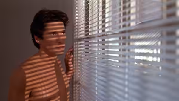 Julian Kaye (Richard Gere) peers through venetian blinds, striped sunlight falling across his bare chest