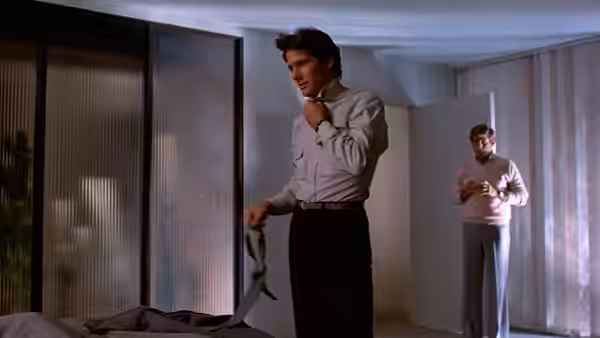 Julian Kaye (Richard Gere) stands beside a bed holding a garment as another man watches