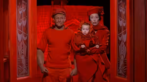 Popeye (Robin Williams) and Olive Oyl (Shelley Duvall) stand with their baby in a red doorway