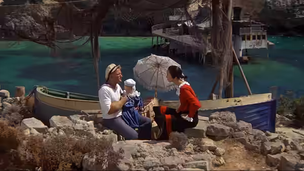 Popeye (Robin Williams) and Olive Oyl (Shelley Duvall) sit beside a boat with their baby