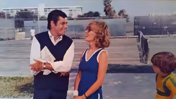Bo Hooper (Jerry Lewis) talking with a woman beside a tennis court as a child watches