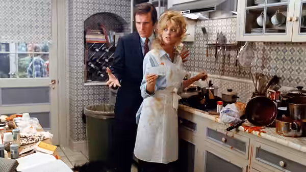 Glenda Parks (Goldie Hawn) cooks in a cluttered kitchen as Nick Gardenia (Chevy Chase) stands behind her