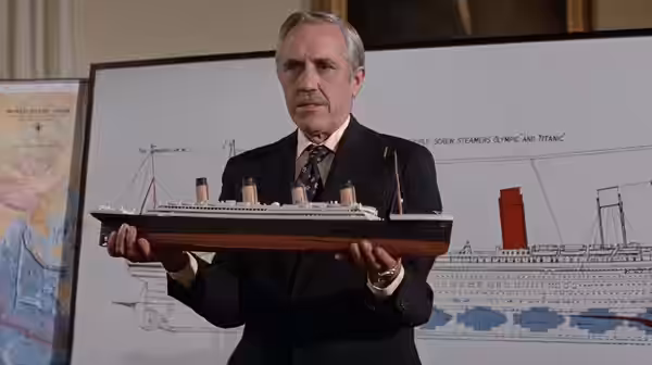Admiral James Sandecker (Jason Robards) presents a model ocean liner before ship blueprints