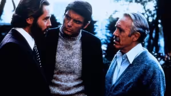 Three men confer outdoors, with an older man listening to the two younger men