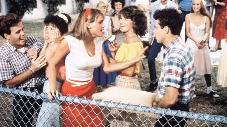 Teenagers gather around a chain-link fence as a young woman gestures toward another girl