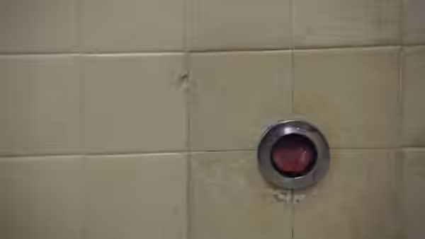 A small red object protrudes through a circular opening in tiled wall