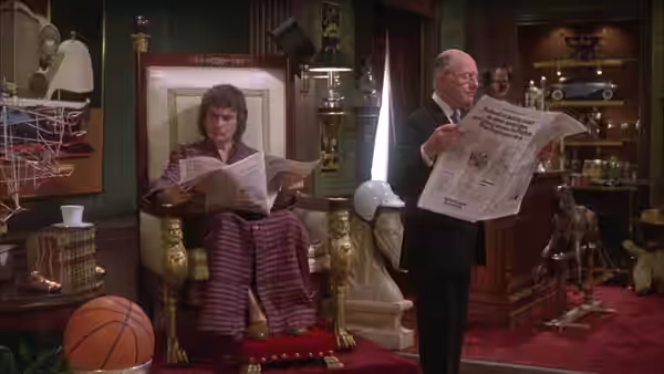 Arthur Bach (Dudley Moore) reads a newspaper while Hobson (John Gielgud) stands nearby
