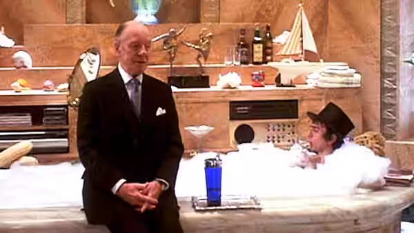 Hobson (John Gielgud) stands beside Arthur Bach (Dudley Moore), relaxing in a bathtub