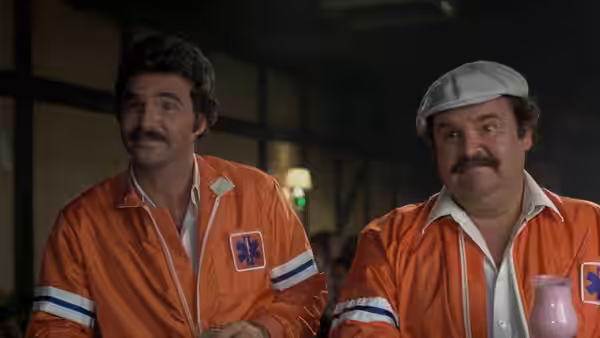 J.J. McClure (Burt Reynolds) and Victor (Dom DeLuise) sit in orange racing uniforms