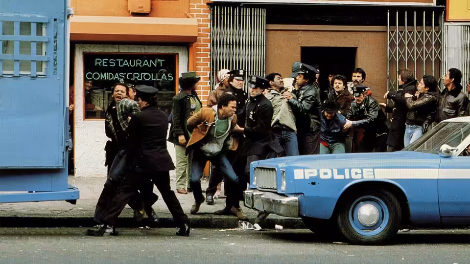 Police officers and residents gather beside a patrol car outside a neighborhood restaurant
