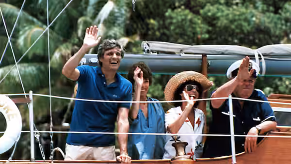 Four friends wave from the deck of a sailboat