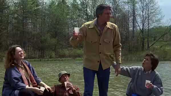 Friends gather beside a pond as a standing man raises his drink
