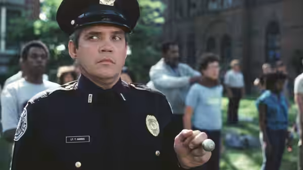 Lieutenant Harris (G. W. Bailey) holds a small object while looking sideways in a courtyard