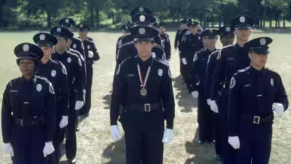 Carey Mahoney (Steve Guttenberg) stands at the front of a police cadet graduation formation