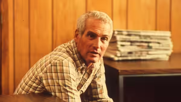 Michael Colin Gallagher (Paul Newman) leans forward in a wood-paneled room